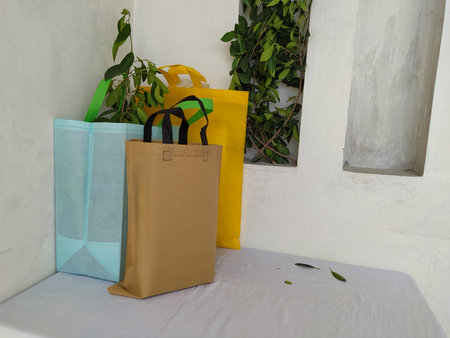 Assorted Color Non Woven Bags with green leaves isolated on white desk. ECO Friendly Shopping bags for mock-up. Copy space Concept for text. New Year and Christmas Gift Bags.の写真素材