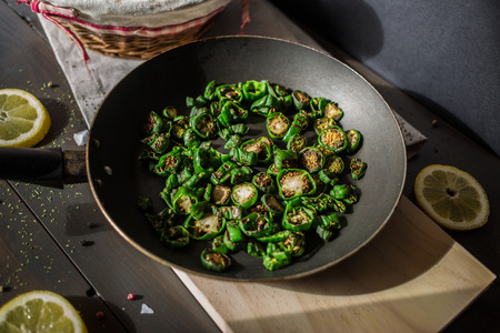 Tasty fried green pepper on a black dish on a table of dark wood, with slices of lemon and saltの写真素材