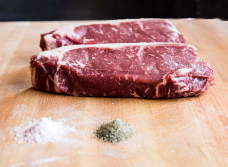Raw meat steaks of various cuts on a butcher block ready to be barbecued grilling hamburgers with seasoning salt and pepper and rosemary garnish farm fresh from Montanaの写真素材