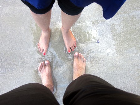 a couple romantically standing on the beach with only their feet being visible.  Romance at its best.の写真素材