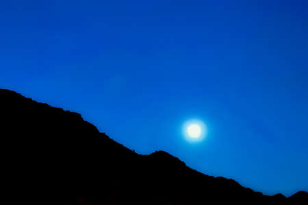 Moonlit night at Sahara desert beside a mountainの写真素材