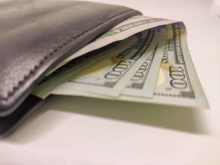 Closeup black wallet full of 100 dollar bills isolated on white background.
