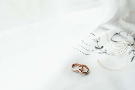 wedding rings of gold on a white table near white curtainの写真素材