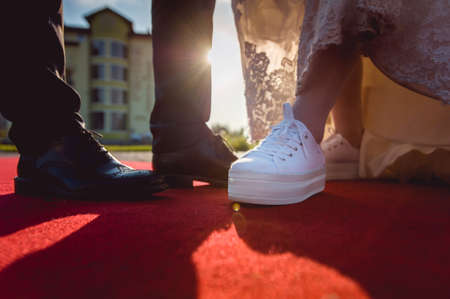 groom in classic  shoes, bride in sneakers. on the red carpet in backlitの写真素材