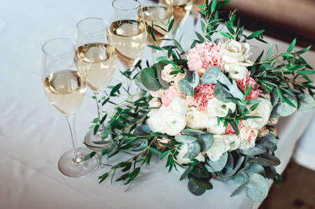 wedding bouquet of white and biege with a ribbon on the table with six glasses of champagneの写真素材