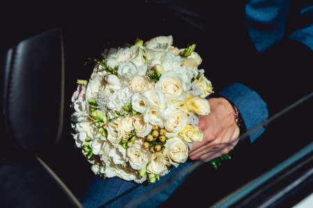 fiance in a dark blue suit sitting in a car with a wedding bouquet made of white rosesの写真素材