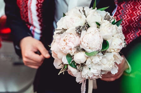 fiance in a dark shirt holding a wedding bouquet made of white peonyの写真素材