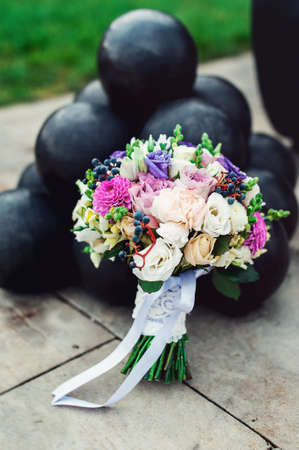 bridal bouquet of different flowers wrapped lace ribbon near bunch of cannonballsの写真素材