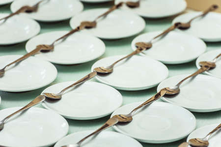 Rows of clean white dish and spoon in a cafeteria or restaurant ready to serveの写真素材