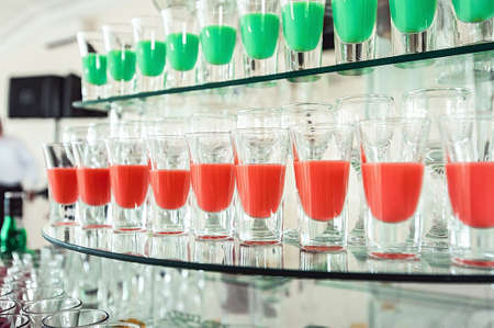 Variety of colorful green and red alcohol shots in small glasses standing in row on a glass stand