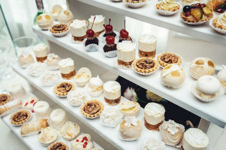 Wedding reception stand with sweets, candies, dessert, cupcakes, muffins, cakes, eclairs decorated with flowersの写真素材
