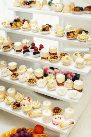 Wedding reception stand with sweets, candies, dessert, cupcakes, muffins, cakes, eclairs decorated with flowersの写真素材