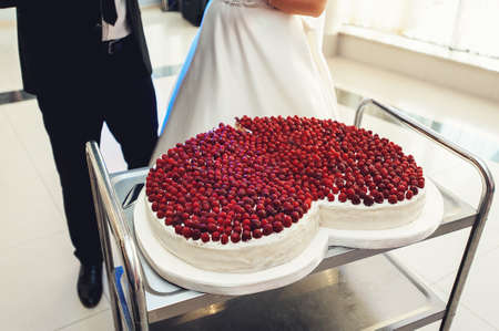 bride and groom prepairing for cutting big wedding cake in the shape of heart. On top its covered...