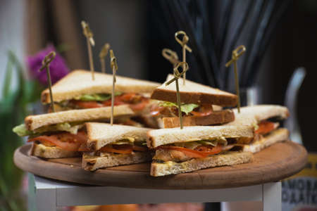 Fresh club sandwiches triangular form with tomato on a round wooden chopping board on a table in a expencive restaurantの写真素材