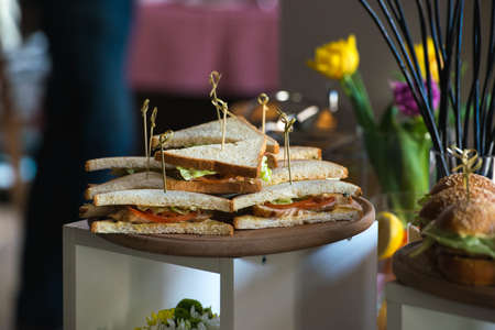 Fresh club sandwiches triangular form with tomato on a round wooden chopping board on a table in a expencive restaurantの写真素材