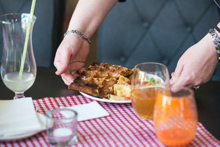 woman is going to eat Belgian waffles, brunch in a restaurant. plate in handの写真素材
