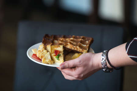 woman is going to eat Belgian waffles, brunch in a restaurant. plate in handの写真素材
