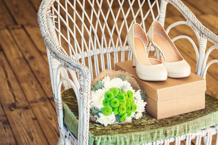 Beautiful wedding shoes with high heels and a bouquet of white and green flowers on a vintage chair in sun light, decorations, preparing for the wedding, details, boudoir, craftboxの写真素材