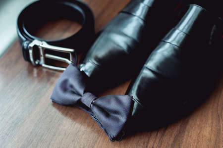 Black bow tie lies before leather shoes and belt. Grooms wedding morningの写真素材