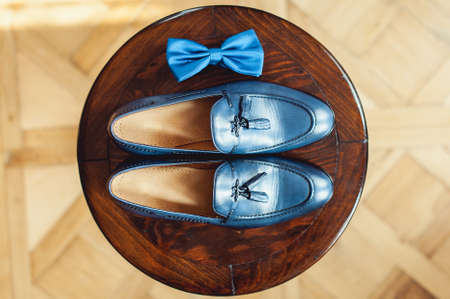Blue shoes and bow tie on a wooden round stool. Accessory for formal dress. Symbol of elegance and fashion for men.の写真素材