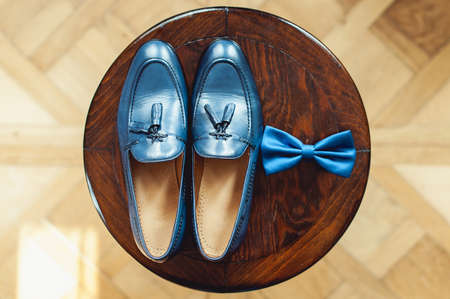 Blue shoes and bow tie on a wooden round stool. Accessory for formal dress. Symbol of elegance and fashion for men.の写真素材