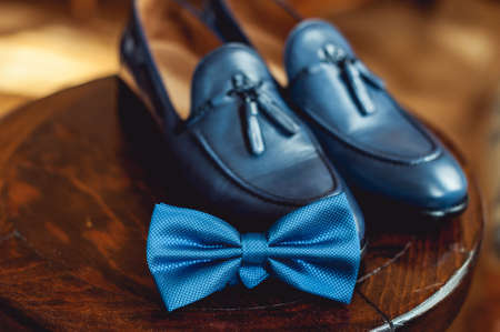 Blue shoes and bow tie on a wooden round stool. Accessory for formal dress. Symbol of elegance and fashion for men.の写真素材