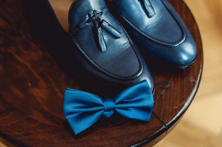 Blue shoes and bow tie on a wooden round stool. Accessory for formal dress. Symbol of elegance and fashion for men.の写真素材