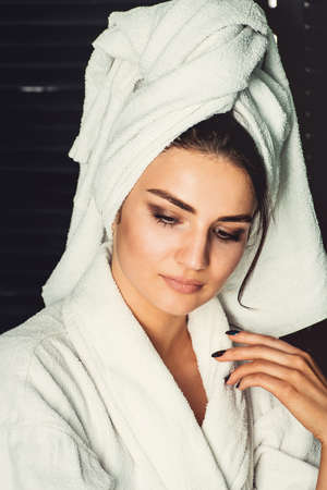 sexy young girl with dark hair, big eyes and dark eyebrows wearing white bath robe whith towel on her head.の写真素材