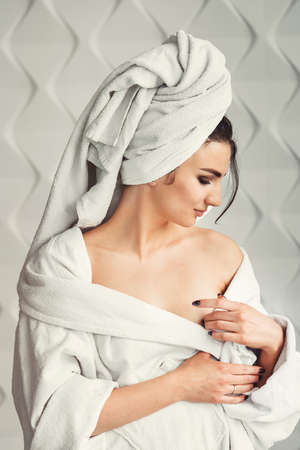 sexy young girl with dark hair, big eyes and dark eyebrows wearing white bath robe whith towel on her head.の写真素材