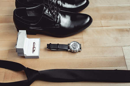 Close up of modern groom accessories. wedding rings, black necktie, leather shoes and watchの写真素材