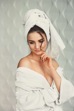 sexy young girl with dark hair, big eyes and dark eyebrows wearing white bath robe whith towel on her head.の写真素材