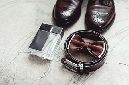 Brown bow tie, perfume, leather shoes and belt. Grooms wedding morning. Close up of modern man accessoriesの写真素材