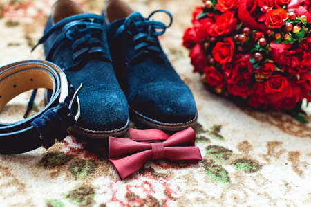 Close up of modern man accessories. Cherry bow tie, blue leather shoest and red wedding bouquet on a carpet.の写真素材