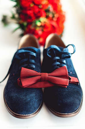 Close up of modern man accessories. Cherry bow tie, blue leather shoest and red wedding bouquet on a carpet.の写真素材
