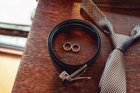 Close up of modern groom accessories. wedding rings, necktie, leather shoes and beltの写真素材