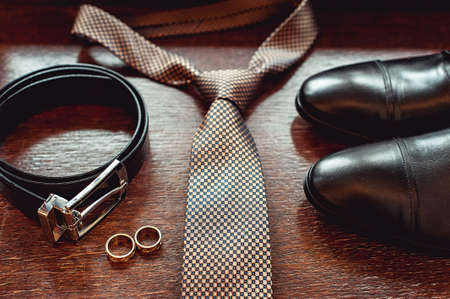 Close up of modern groom accessories. wedding rings, necktie, leather shoes and beltの写真素材