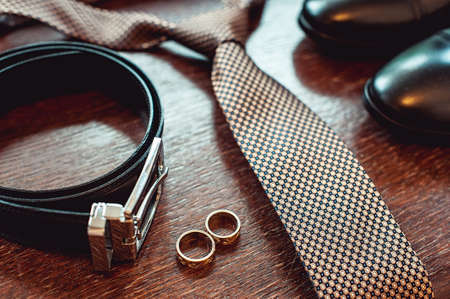 Close up of modern groom accessories. wedding rings, necktie, leather shoes and beltの写真素材