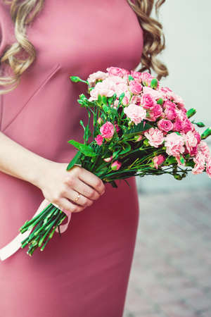 woman in a dress holding wedding bouquets of biege carnations and pink rosesの写真素材