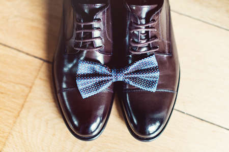 blue bow tie on a leather brown shoes. Grooms wedding morning. Close up of modern man accessories. Look from aboveの写真素材