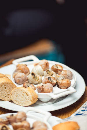 Snails with herbs butter, in traditional ceramic pan with cut parsley, bread and and parsley sauce on textile napkin over rustic wooden table. Top view. restaurant food and wine tastingの写真素材