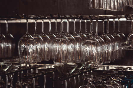 raws of glasses for a margarita, martini, grog and liqueur hanging upside down in bar at arestaurant, dark backgroundの写真素材