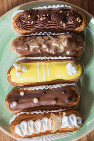 Eclairs with different ganache and icing with different toppings on a plate. View from above