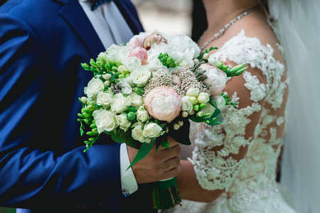 fiance in a dark blue suit holds a wedding bouquet made of peoniesの写真素材