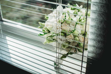 wedding bouquet of white roses on a window sill with jalousieの写真素材