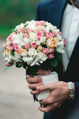 fiance in a dark blue suit holds a wedding bouquet made of white flowersの写真素材