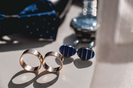 Wedding rings. Black leather shoes, watch, blue bow tie and cufflinks, on a white window sill.
