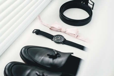 Close up of modern man accessories. beige bow tie, black leather shoes, belt and watch