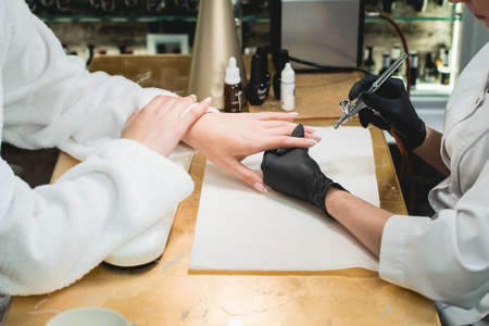 Closeup shot of a woman in a nail salon receiving a manicure by a beautician with airbrush. Woman getting nail manicure.の写真素材