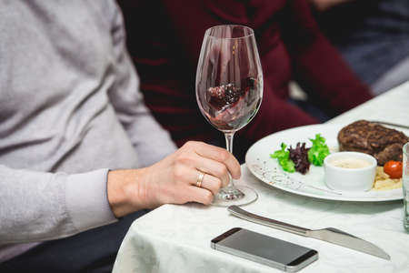 wine tasting in a restaurant. man holds glass of white wine. fresh grilled bbq roast beef steak and sauce on a white plate with green leaf of salad.の写真素材
