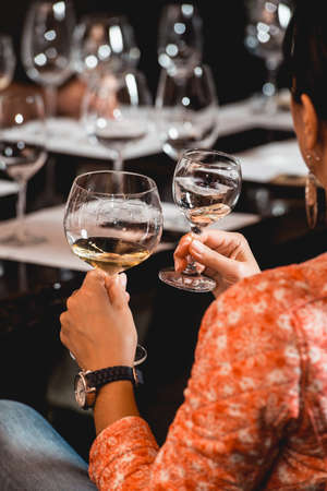 woman holds two glasses of white wine. people consider the color of the wine and try how it smells...